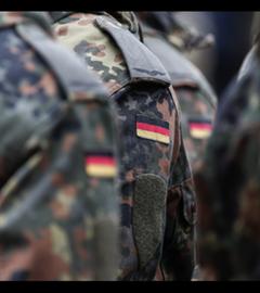 Die aneinandergereihten Schultern von uniformierten Bundeswehrsoldat:innen mit der deutschen Fahne.