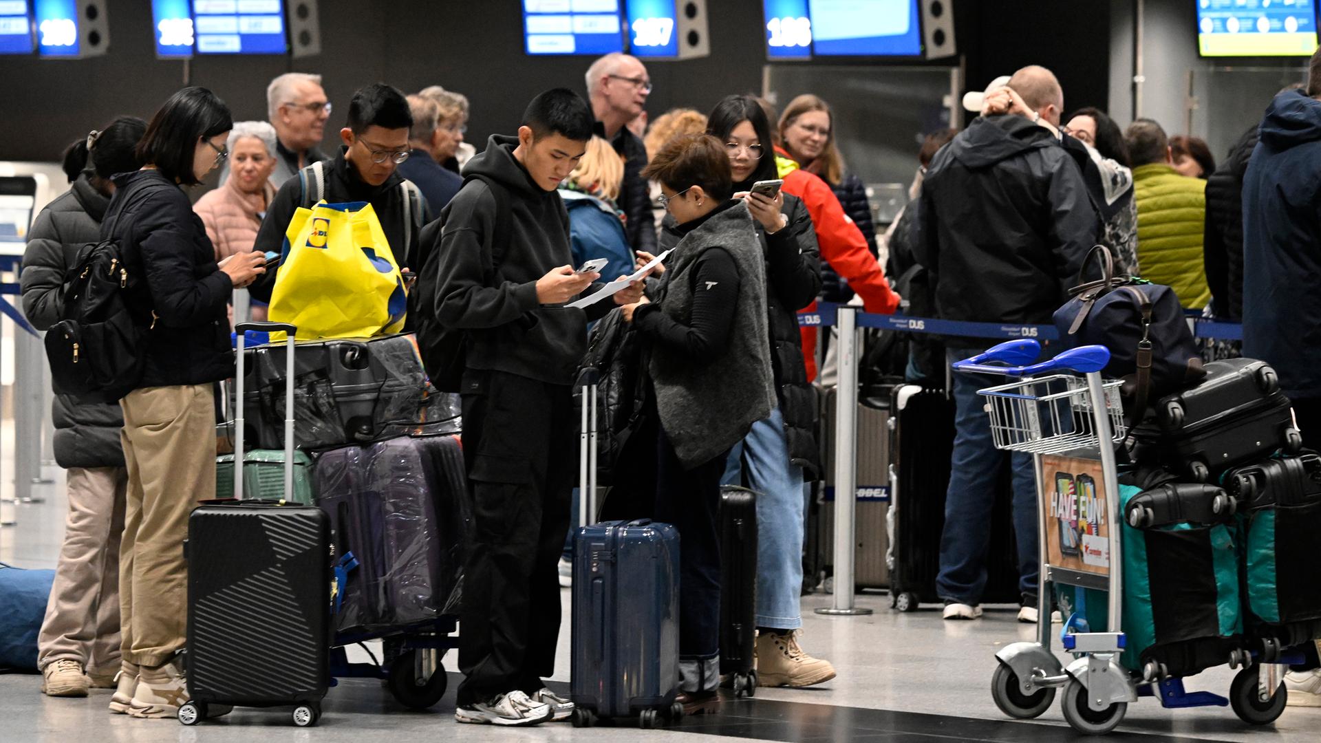  Reisende bilden am Flughafen beim Check-In eine Schlange.