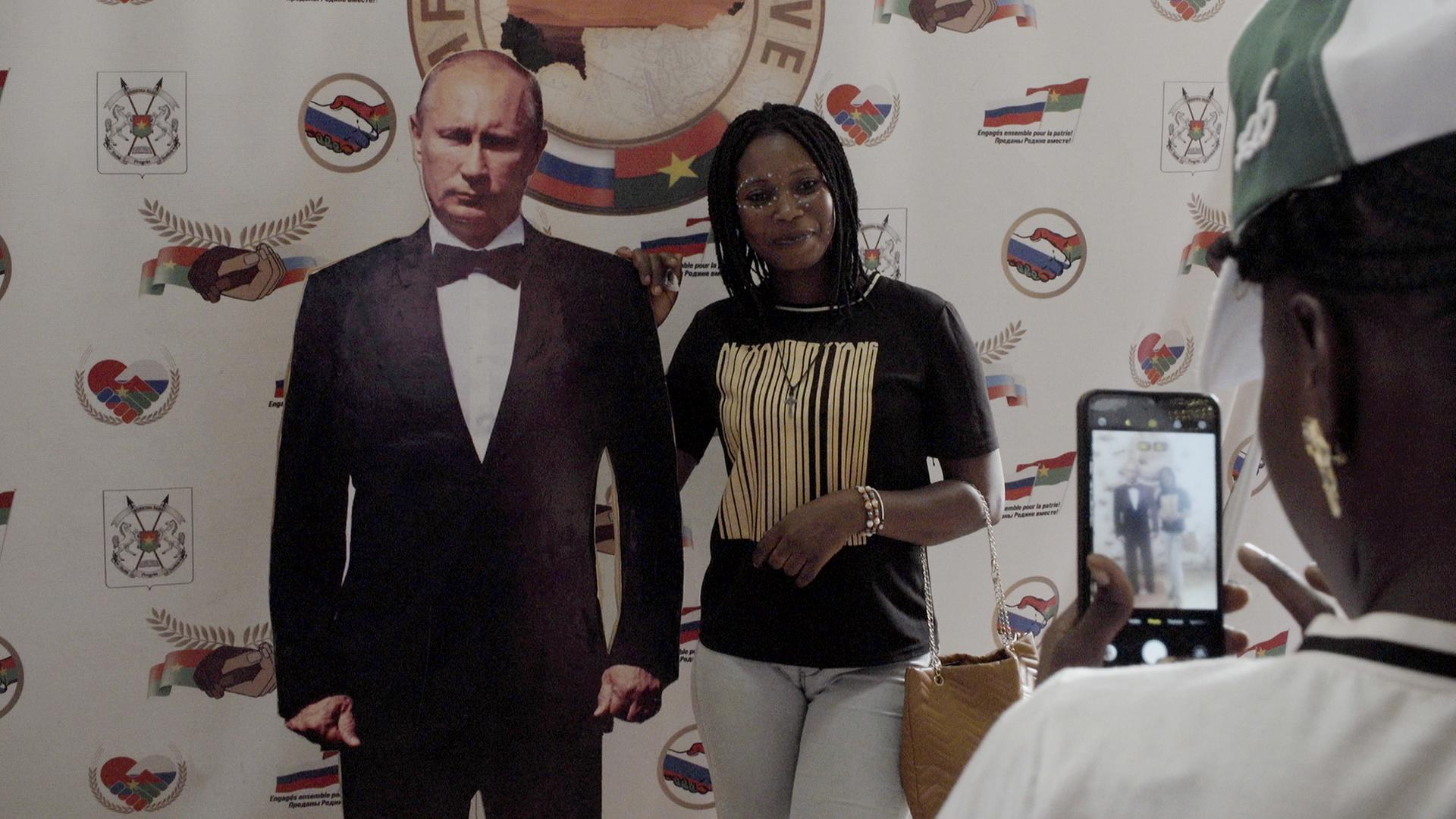 Eine Frau posiert neben einer Figur von Wladimir Putin.