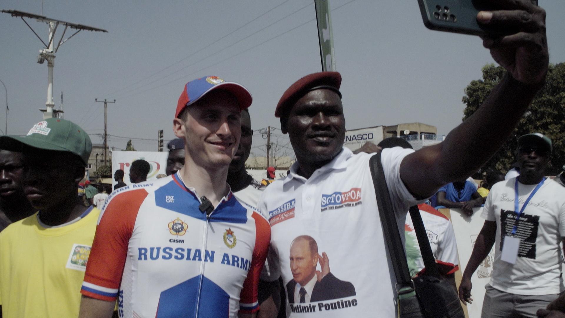 Eine Person im Putin-Tshirt macht ein Selfie mit einem russischen Radfahrer. 