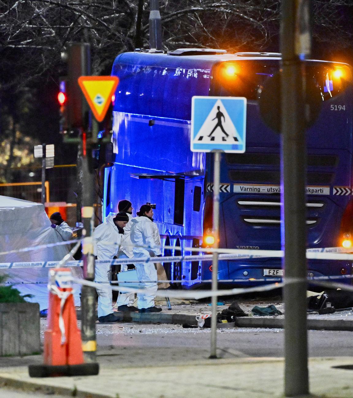 Einsatzkräfte in Schutzanzügen stehen an der Unfallstelle, an der ein Doppeldeckerbus in ein Wartehäuschen krachte und dabei Tote und Verletzte am 14.11.2025 im schwedischen Stockholm forderte.