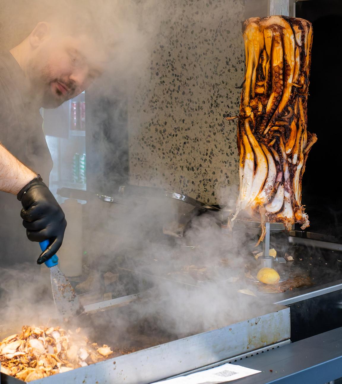 07.11.2025, Baden-Württemberg, Karlsruhe: Ein Mitarbeiter bereitet im Restaurant "Pescobar" das Fleisch für einen Calamari-Kebab zu.