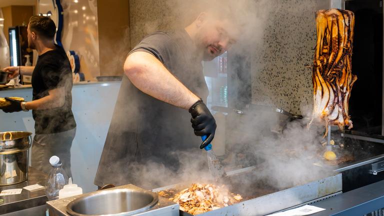 07.11.2025, Baden-Württemberg, Karlsruhe: Ein Mitarbeiter bereitet im Restaurant "Pescobar" das Fleisch für einen Calamari-Kebab zu.