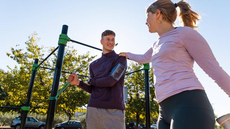 Eine Frau und ein Mann trainineren an einem öffentlichen Calisthenics-Gerät in einem Park.