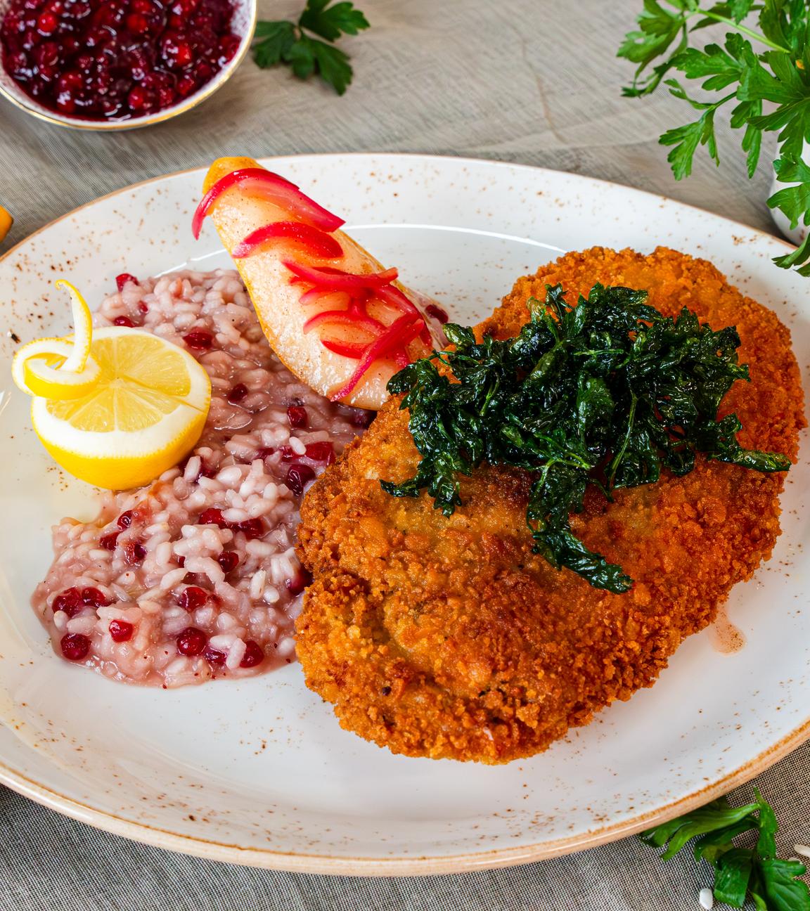 Putenschnitzel mit Camenbert gefüllt, mit frittierter Petersilie getoppt, daneben Preiselbeer-Risotto und gebratene Birnenscheibe.