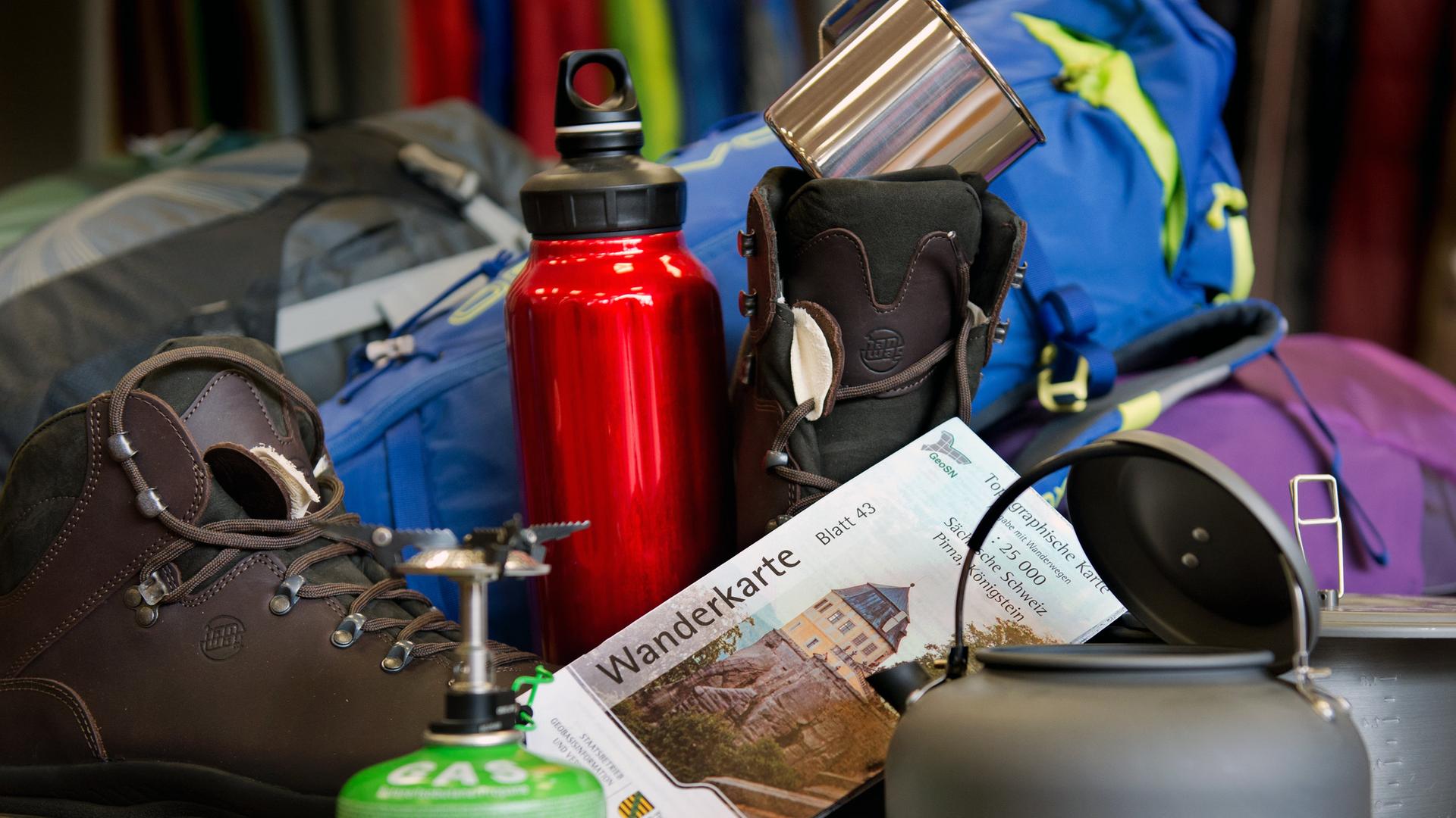 Verschiedene Dinge wie Becher, Trinkflasche oder Gaskocher, die für Wander- und Campingausrüstung notwendig sind.