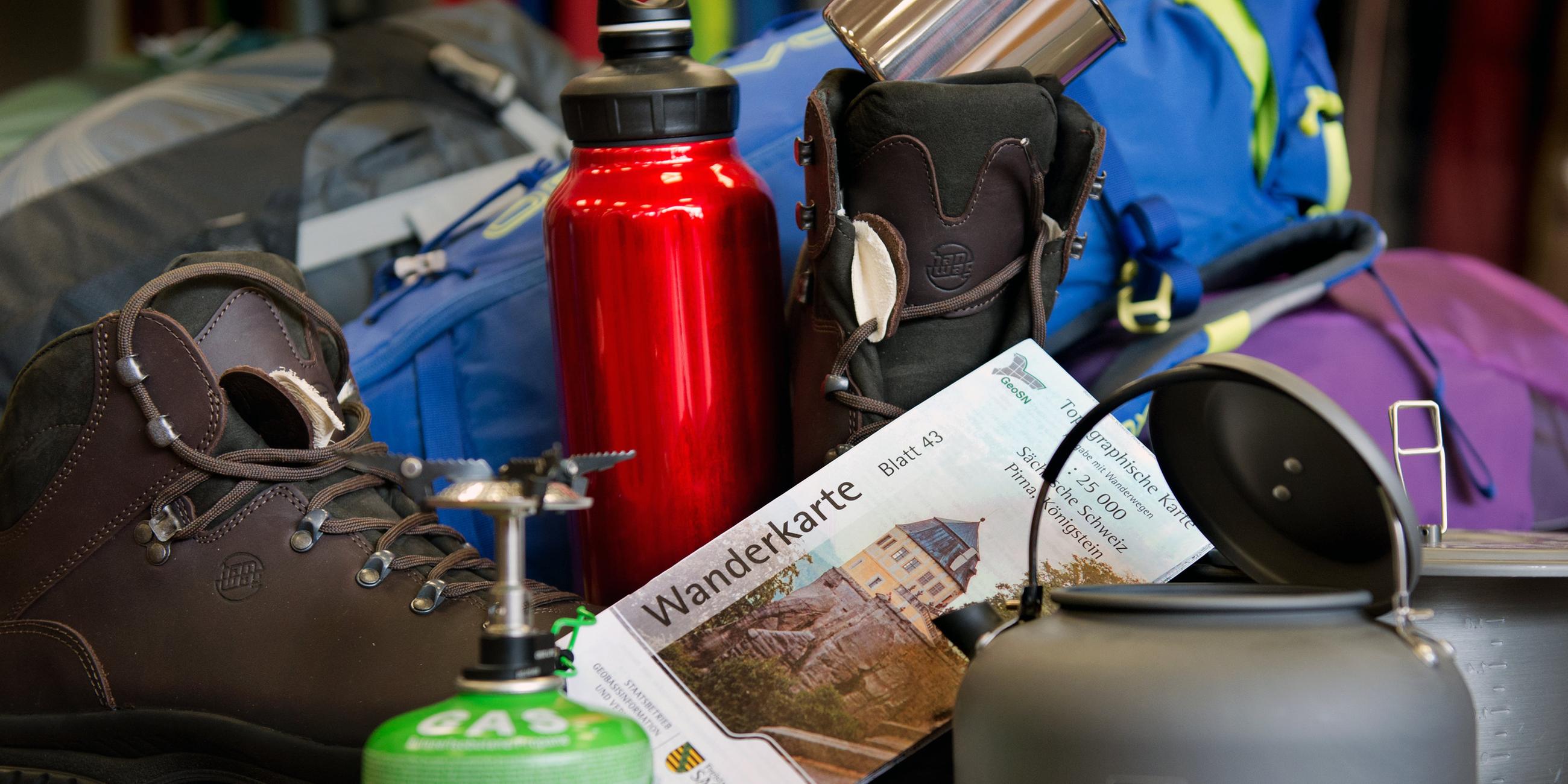 Verschiedene Dinge wie Becher, Trinkflasche oder Gaskocher, die für Wander- und Campingausrüstung notwendig sind.