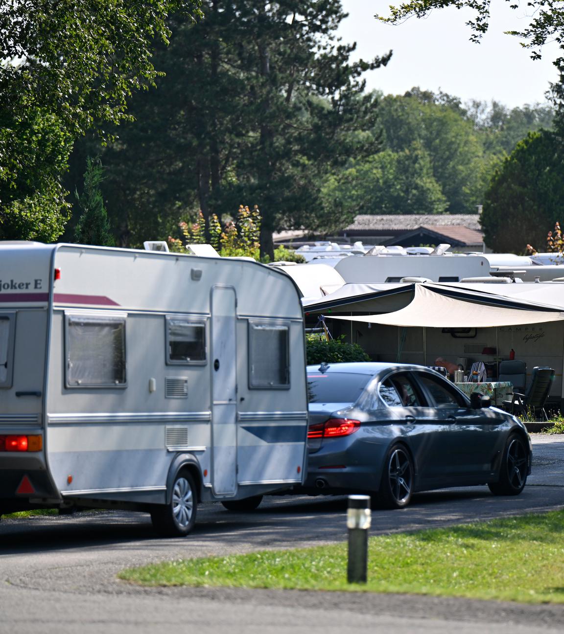 Wohnmobile und Wohnwagen stehen auf einem Campingplatz zwischen Bäumen in Oberbayern.