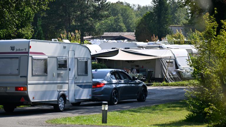 Wohnmobile und Wohnwagen stehen auf einem Campingplatz zwischen Bäumen in Oberbayern.