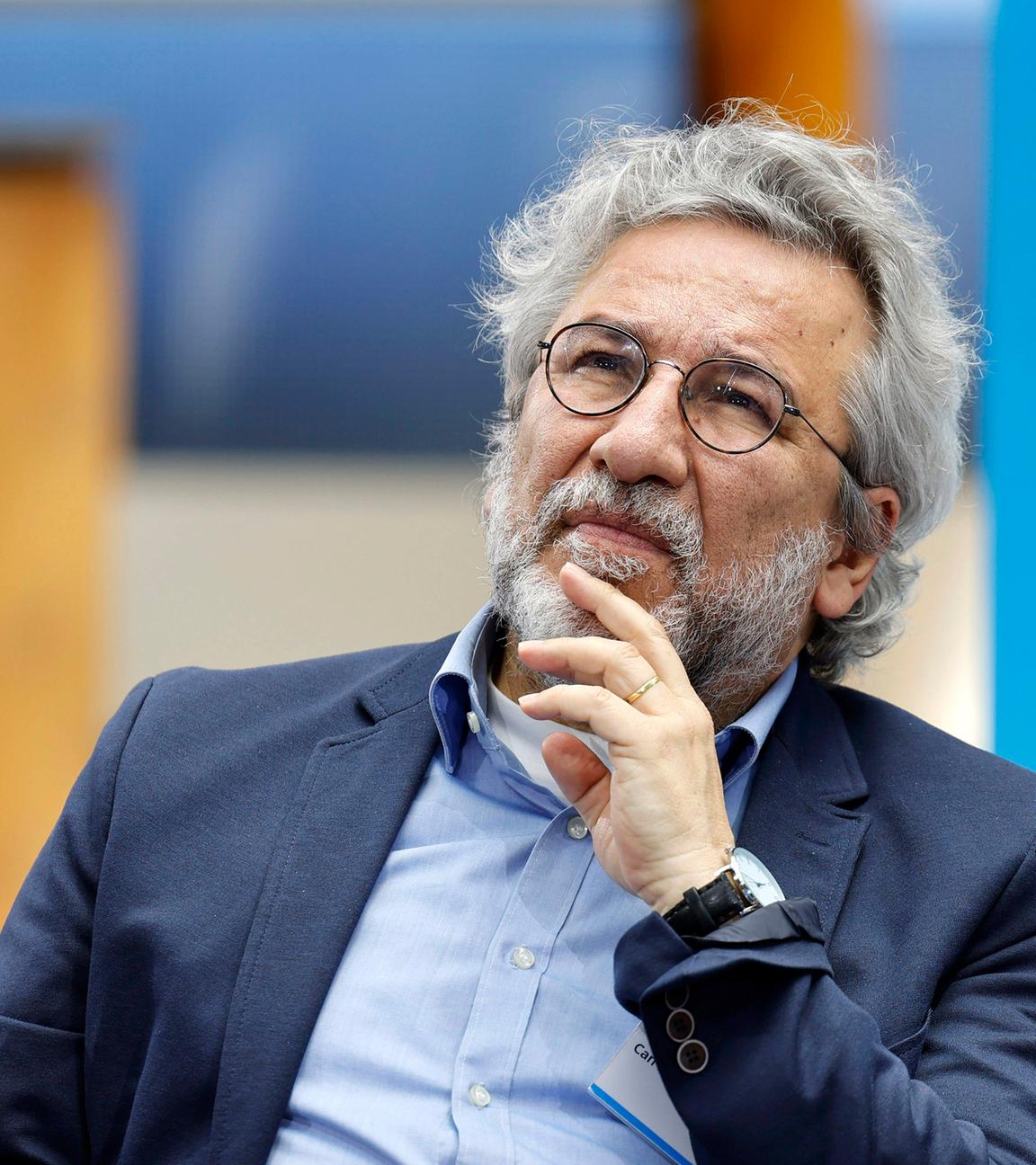 Foto eines Mannes mit weißen Locken, graumeliertem Bart und runder Metall-Brille, der sich nachdenklich mit der Hand ans Kinn fasst.