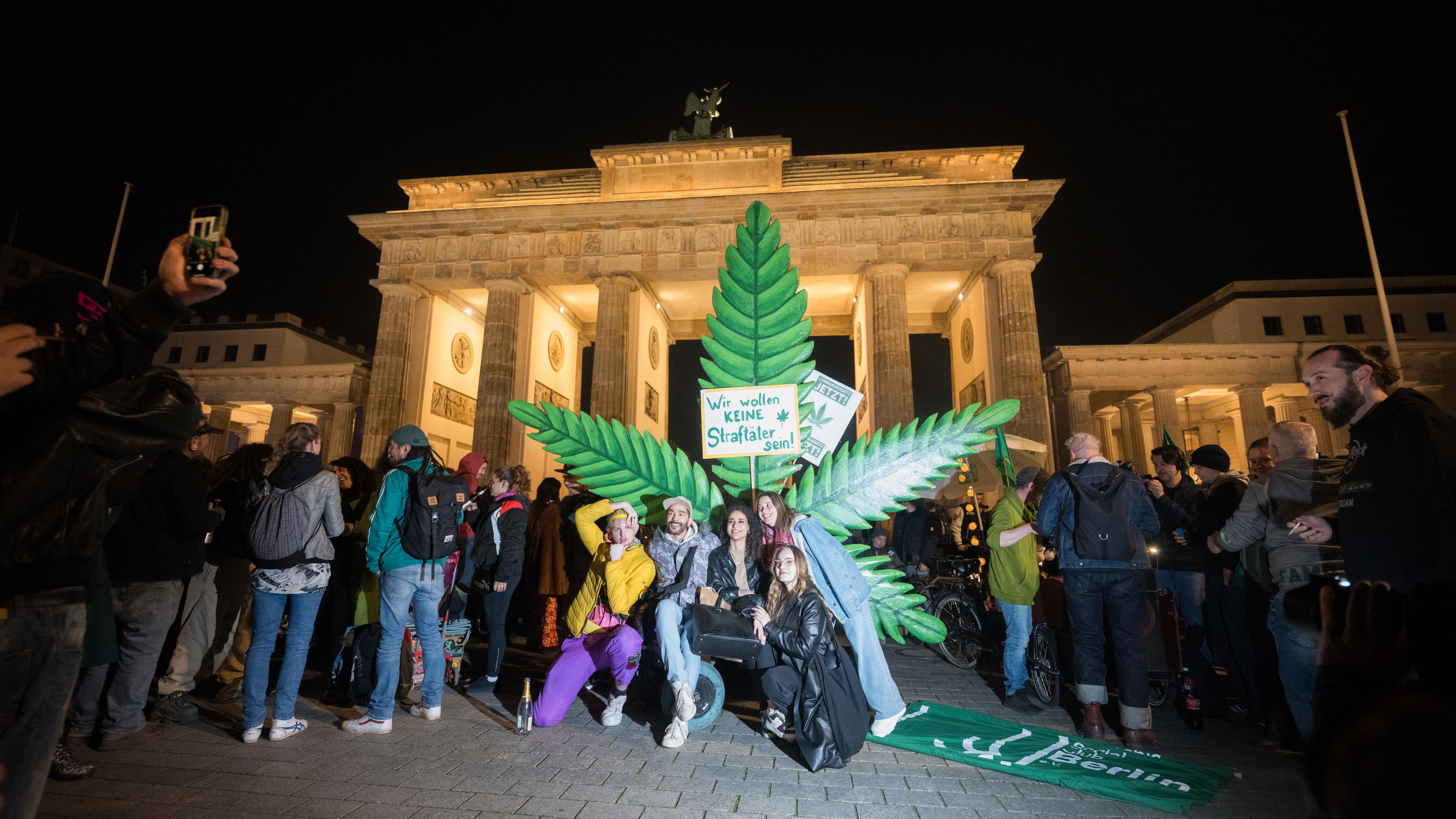 Menschen stehen während eines "Smoke In" vor dem Brandenburger Tor vor einem großen Hanfblatt.