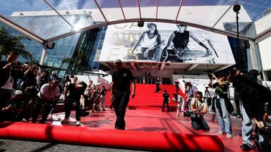 Pressefotografen und Zuschauer machen Fotos, während der rote Teppich vor dem Eingang zum Kino in Cannes ausgerollt wird.