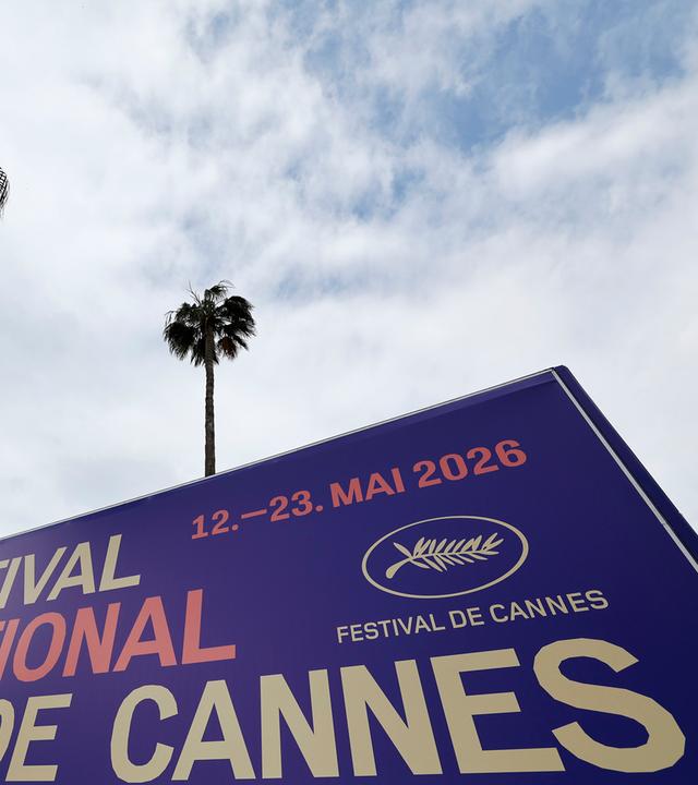 Ein Schild für das Cannes Film Festival, schräg von unten fotografiert, im Hintergrund sind Palmen zu sehen.