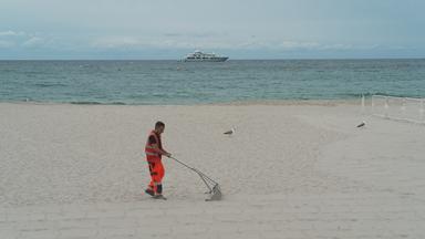 Helfer siebt Müll aus dem Sand am Strand von Cannes