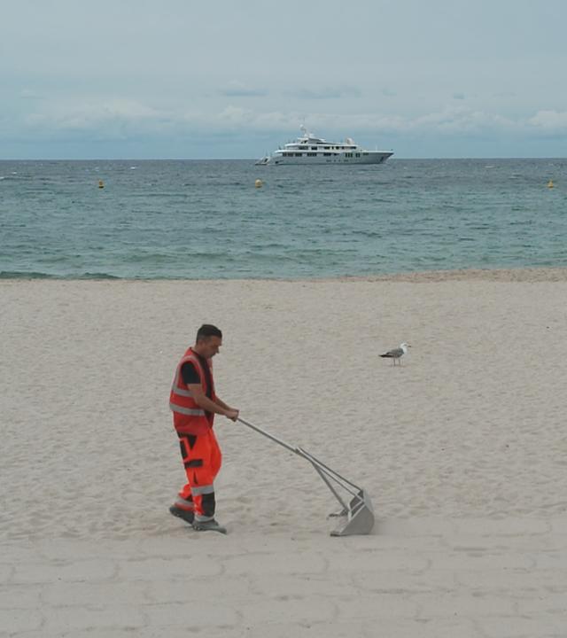 Helfer siebt Müll aus dem Sand am Strand von Cannes