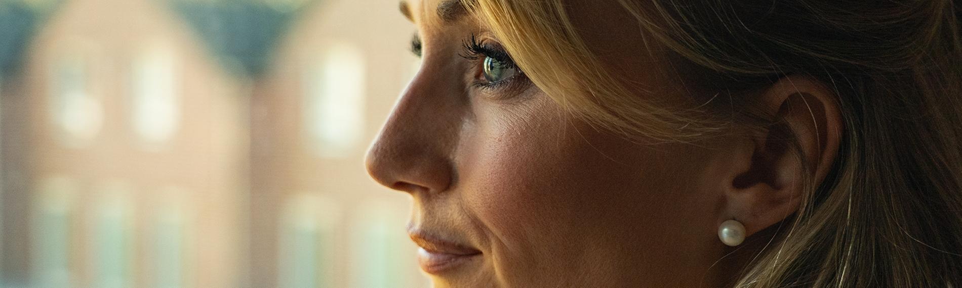  Junge Frau mit blonden, langen Haaren schaut aus dem Fenster.
