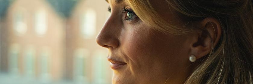  Junge Frau mit blonden, langen Haaren schaut aus dem Fenster.