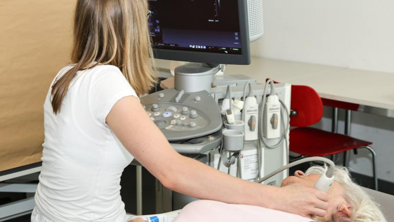 Eine Ärztin macht bei einer Frau eine Ultraschalluntersuchung der Halssschlagader zur Schlaganfallvorsorge.