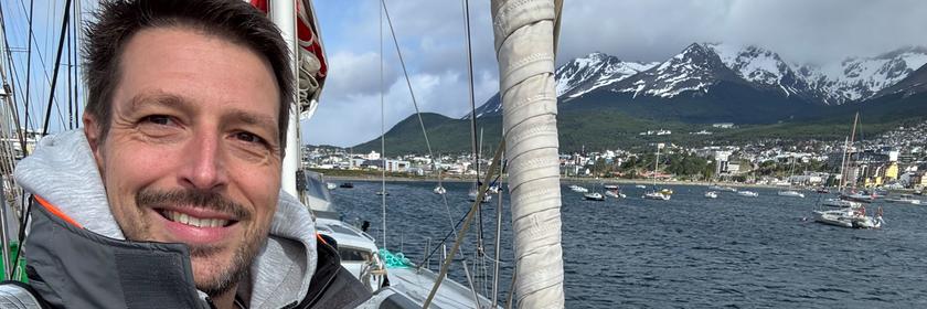 Carsten Behrendt, ein weißer Mann mit kurzen braunen Haaren in grauer Funktionsjacke macht ein Selfie auf einem Segelboot.