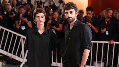 Eine Frau und ein Mann stehen ernst auf dem roten Teppich bei den Filmfestspielen von Venedig. Hinter ihnen sind hinter einer Absprerrung Fotografen zu sehen.