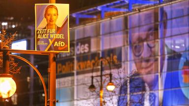AfD-Wahlplakat mit Alice Weidel fuer die Bundestagswahl, im Hintergrund ein Werbebanner an der CDU-Zentrale mit dem Bild von Friedrich Merz.
