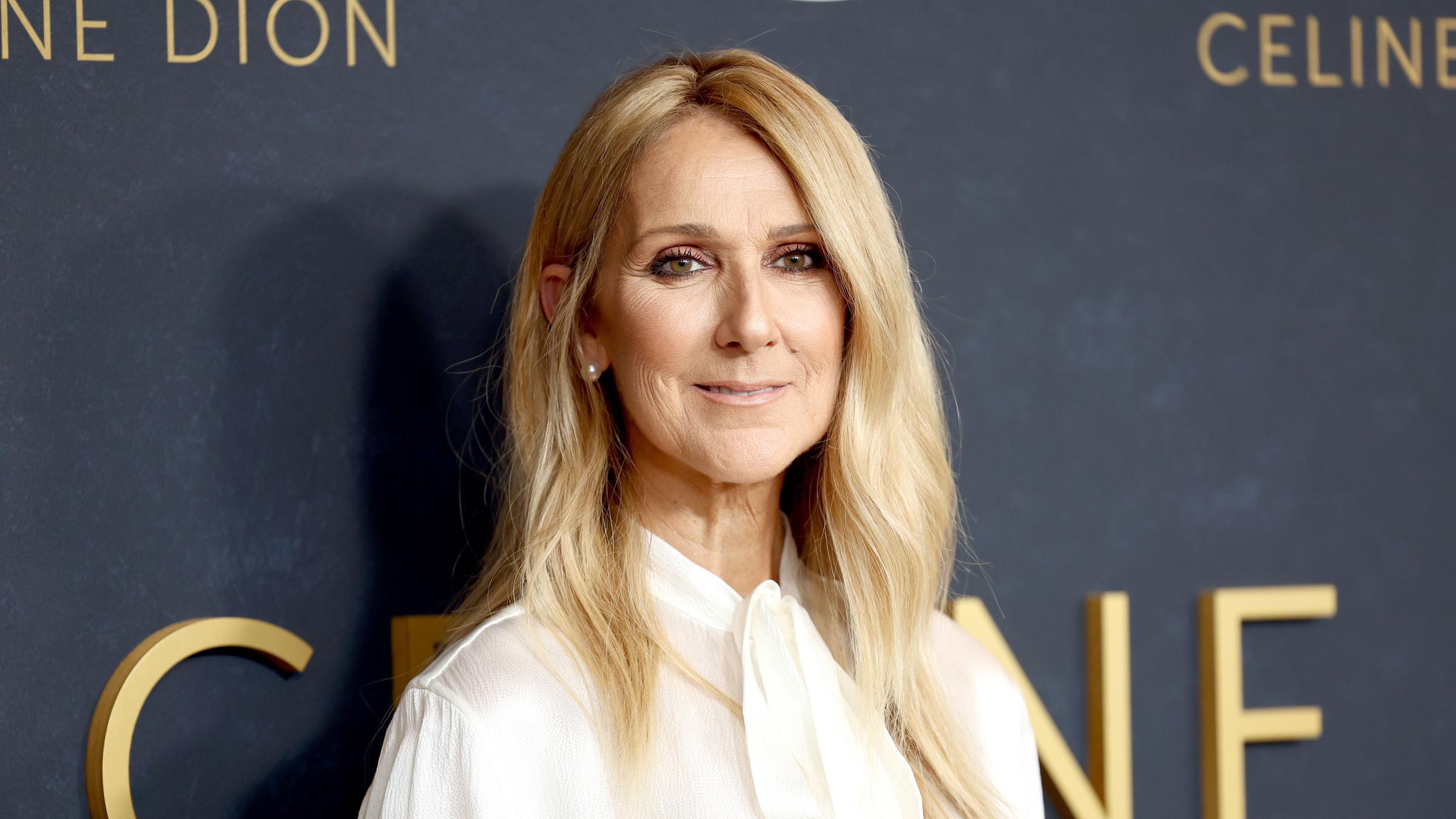 Celine Dion posiert vor einer Wand mit ihrem Namen drauf.