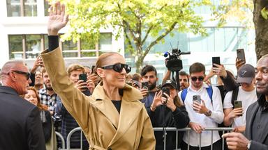 Das BIld zeigt Sängerin Céline Dion, die zahlreichen Fans hinter einem Zaun zuwinkt.