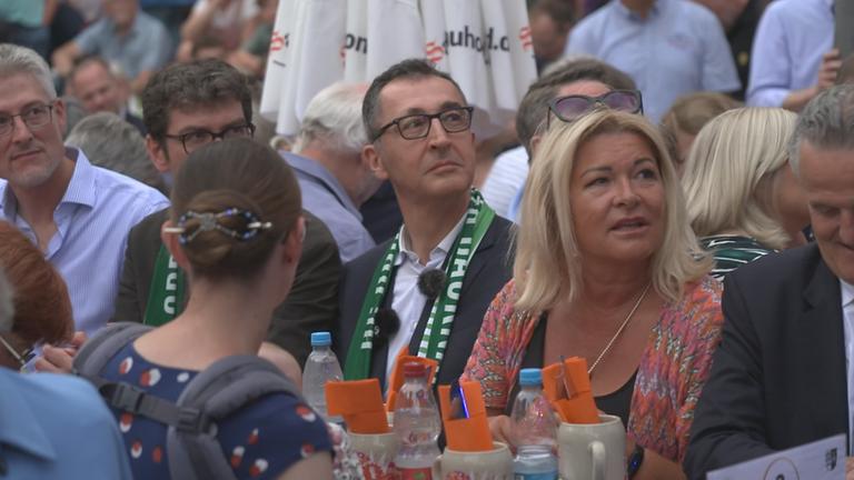 Cem Özdemir sitzt bei Volksfest zwischen vielen Menschen an einem Tisch