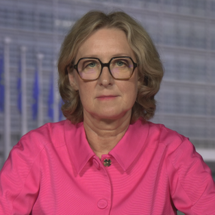 ZDF-Reporterin Susanne Freitag-Carteron in einer pinken Hemd-Jacke in dem Studio in Brüssel. Im Hintergrund sind EU-Flaggen zu sehen.