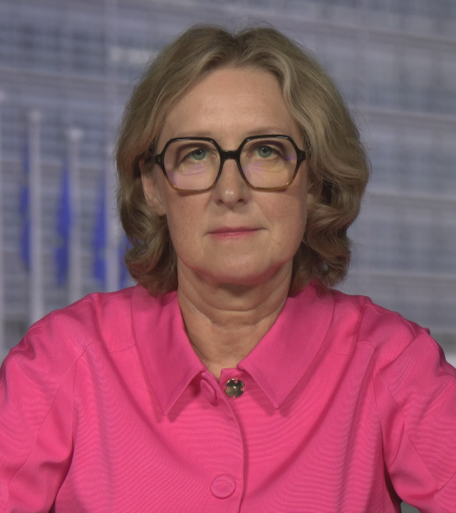 ZDF-Reporterin Susanne Freitag-Carteron in einer pinken Hemd-Jacke in dem Studio in Brüssel. Im Hintergrund sind EU-Flaggen zu sehen.