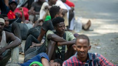 Menschen sitzen vor dem überlasteten Aufnahmezentrum für Migranten.