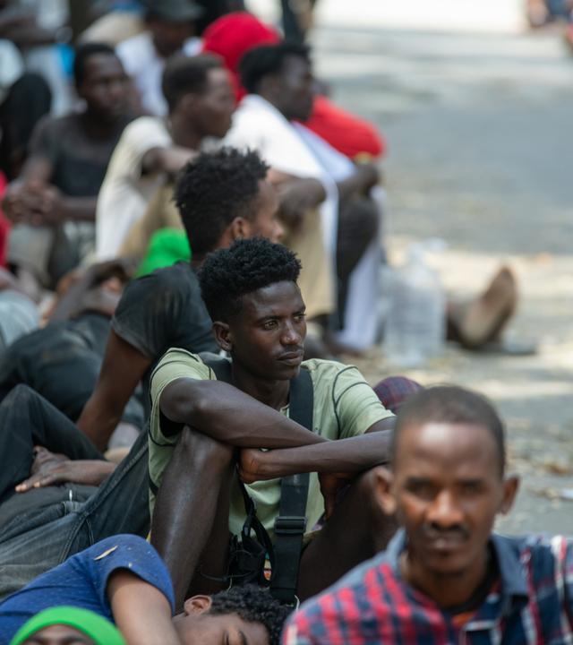 Menschen sitzen vor dem überlasteten Aufnahmezentrum für Migranten.