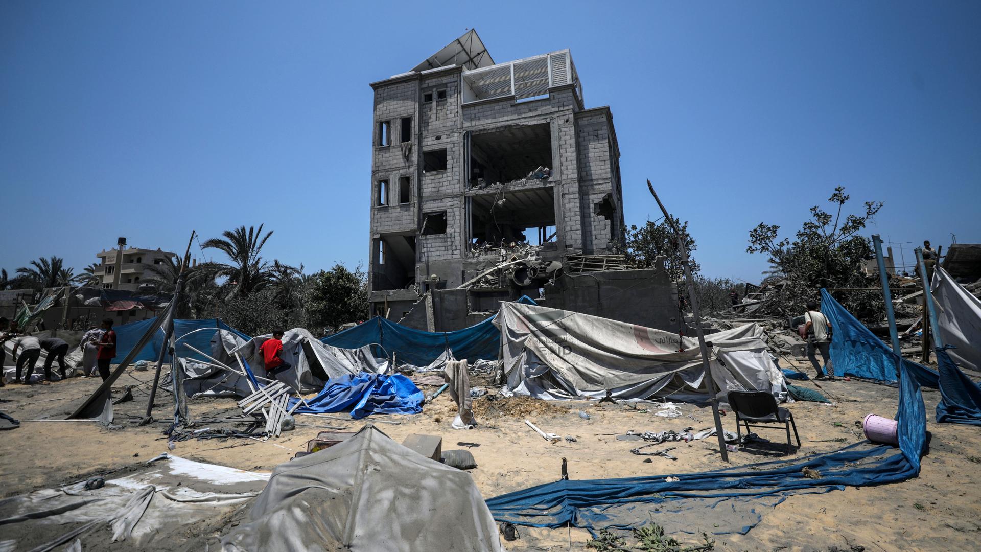 Ein zerstörtes Gebäude im Hintergrund, zerstörte Zelte im Vordergrund in Chan Junis.