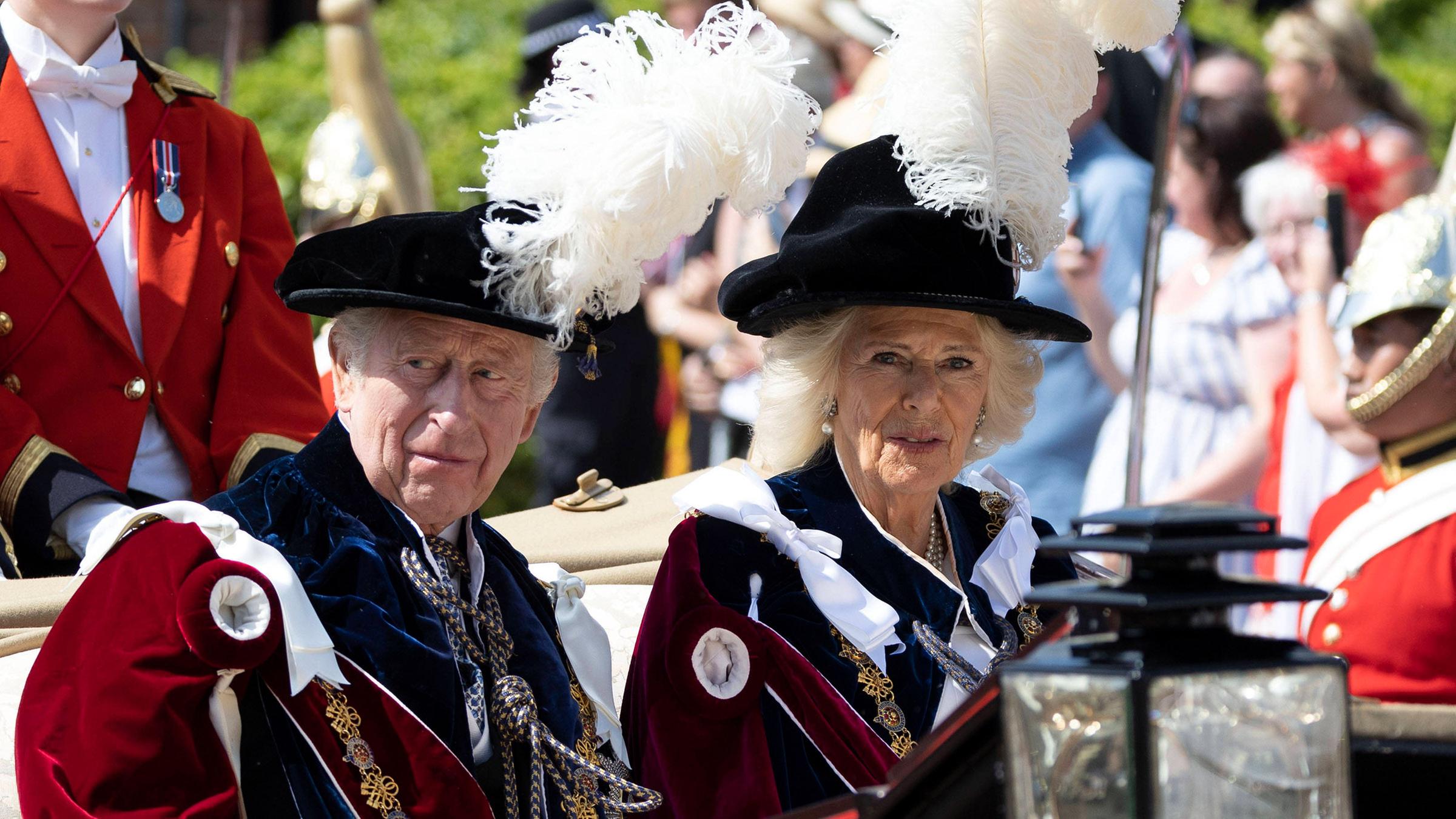 Charles und Camilla werden mit gefederten Hüten in einer Kutsche.