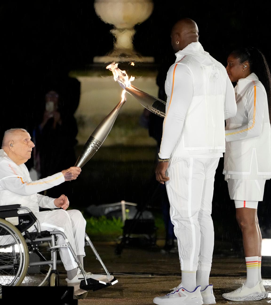 Charles Coste übergibt bei der Eröffnungsfeier der Olympischen Sommerspiele in Paris 2024 im Rollstuhl sitzend das olympische Feuer
