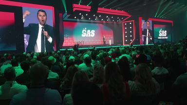 Ein junger Mann im Anzug (Charlie Krik, 31) spricht beim Student Action Summit von einer Bühne, das Publikum schaut ihm zu. 