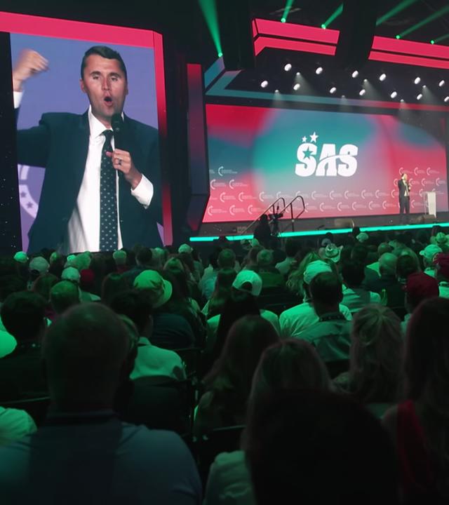 Ein junger Mann im Anzug (Charlie Krik, 31) spricht beim Student Action Summit von einer Bühne, das Publikum schaut ihm zu. 