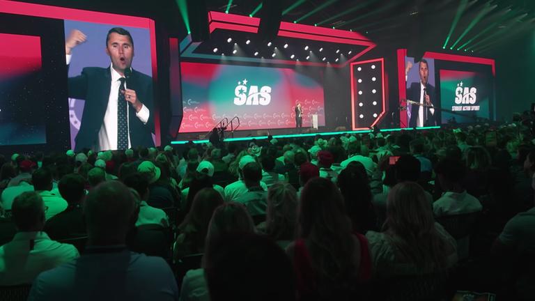 Ein junger Mann im Anzug (Charlie Krik, 31) spricht beim Student Action Summit von einer Bühne, das Publikum schaut ihm zu. 