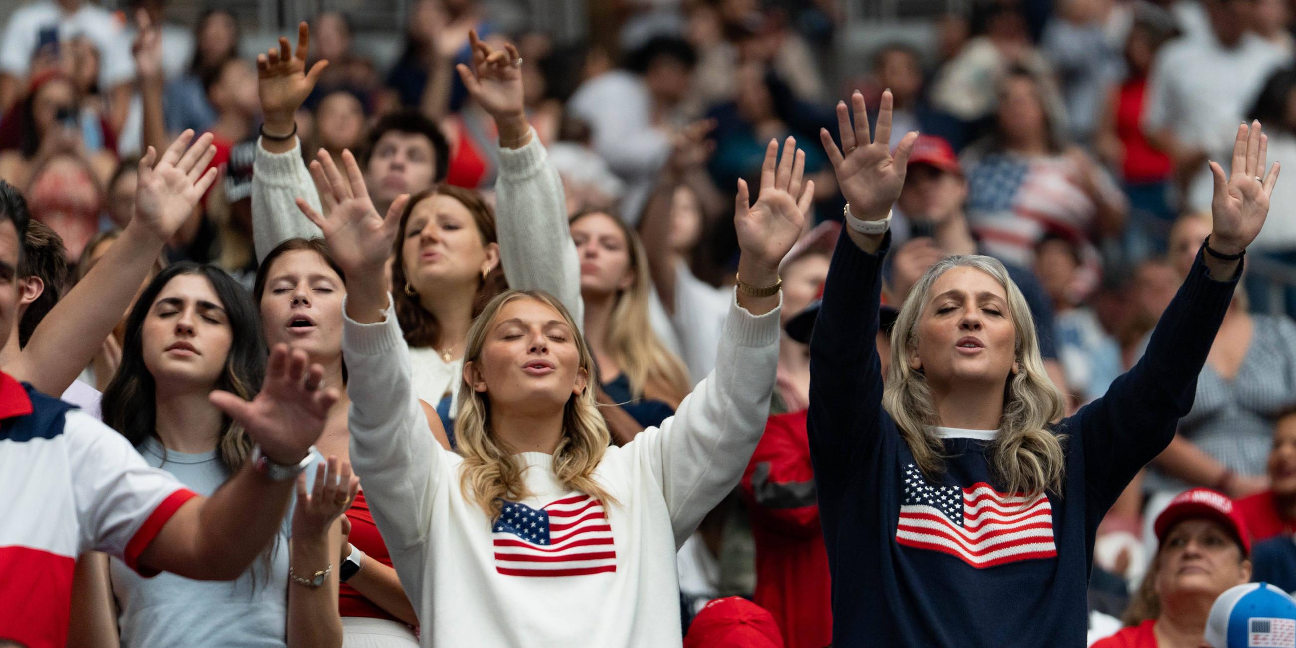Teilnehmer heben die Hände und singen während einer Gedenkfeier für Charlie Kirk im State Farm Stadium in Glendale am 21. Sept. 2025.