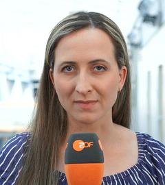 ZDF-Reporterin Charlotte Greipl schaut in die Kamera und hält ein Mikrofon in der Hand.