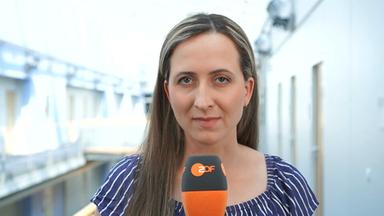 ZDF-Reporterin Charlotte Greipl schaut in die Kamera und hält ein Mikrofon in der Hand.