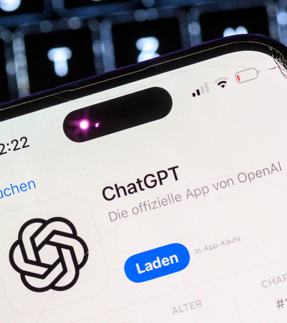 Ein Smartphone mit der App des KI-Chatbots ChatGPT ist vor dem Logo des US-Softwareunternehmens OpenAI zu sehen
