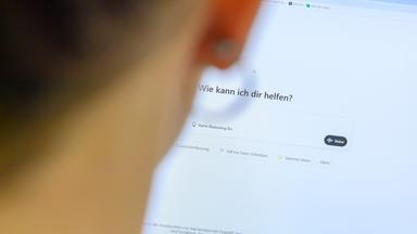 Eine Frau sitzt am Computer und gibt etwas bei "ChatGPT" in die Suchmaske ein.