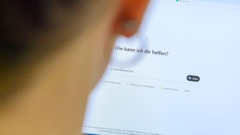 Eine Frau sitzt am Computer und gibt etwas bei "ChatGPT" in die Suchmaske ein.