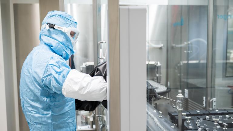 Ein Arbeiter in Schutzkleidung steht an einer Abfüll- und Verschließanlage für pharmazeutische Produkte bei Takeda Pharmaceutical.