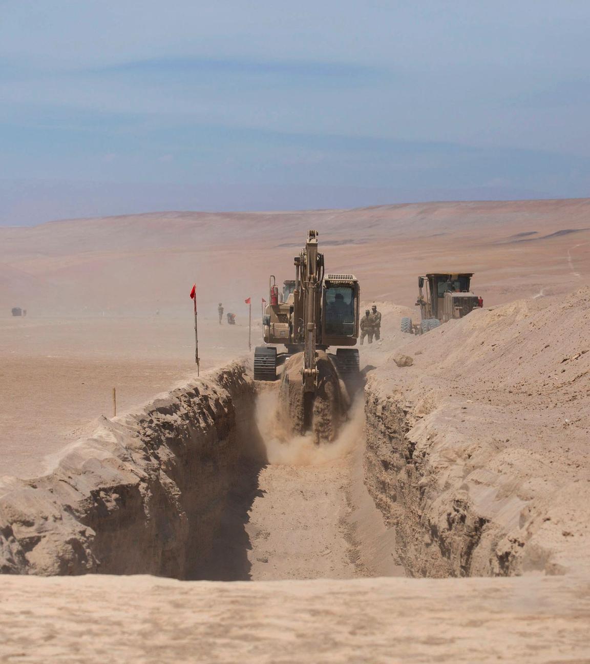 Ein chilenischer Soldat steht Wache während im Hintergrund mit großen Maschinen ein Graben ausgehoben wird, um die Grenze zwischen Chile und Peru zu verstärken.