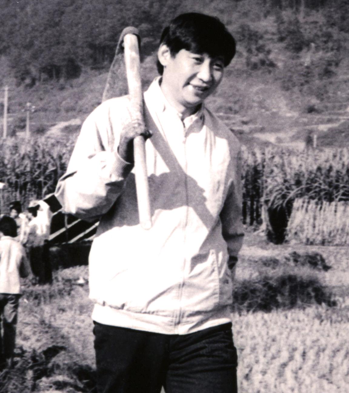 Eine Schwarz-Weiß-Fotoaufnahme von chinesischen Arbeitern, die Schaufeln tragen und in einer Reihe über ein Feld laufen.