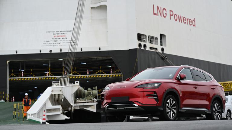 Ein Neuwagen des Modells ·Seal· des chinesischen Autoherstellers BYD steht vor dem Autofrachter BYD Explorer No.1" auf dem der Schriftzug "LNG Powered" zu lesen ist