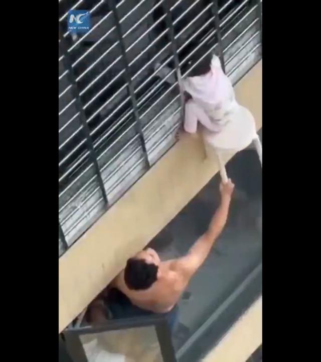 Ein Mann hält ein Kind fest, das aus einem Fenster im 12. Stock geklettert ist. 