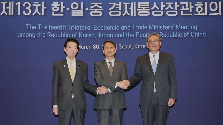 Gelbe Krawatte, braune Krawatte, blaue Krawatte. Drei Männer in dunklen Anzügen. Der in der Mitte überkreuzt die Arme für einen simultanen Handshake mit seinen beiden Nachbarn. Das Foto dieses politischen Treffens sieht unspektakulär aus, doch ist es nicht.